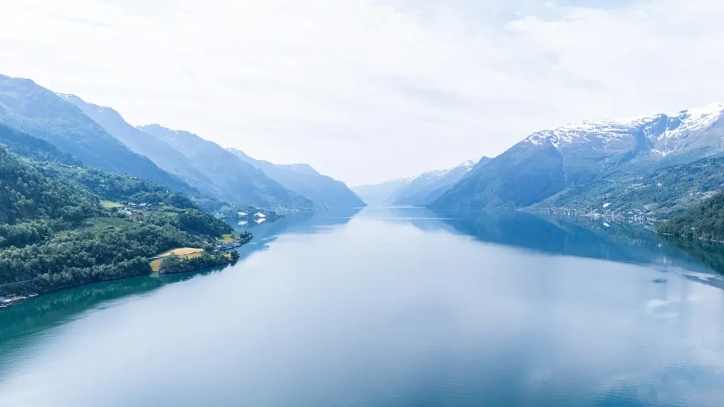 Stille fjord mellom bratte, grønne fjellsider.