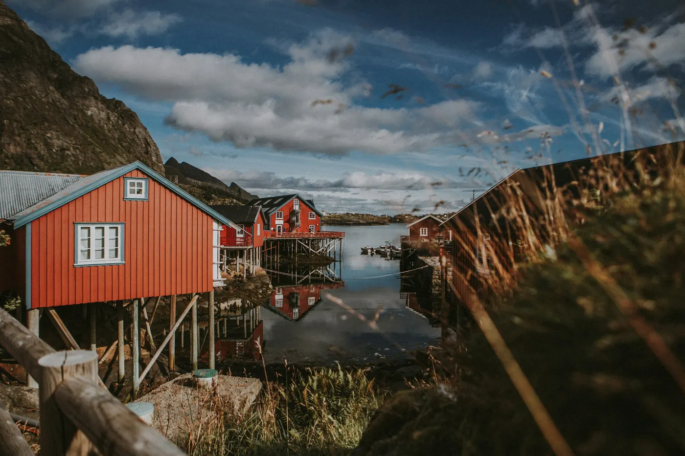 Rødt naust på stolper ved fjorden, med fjell i bakgrunnen.