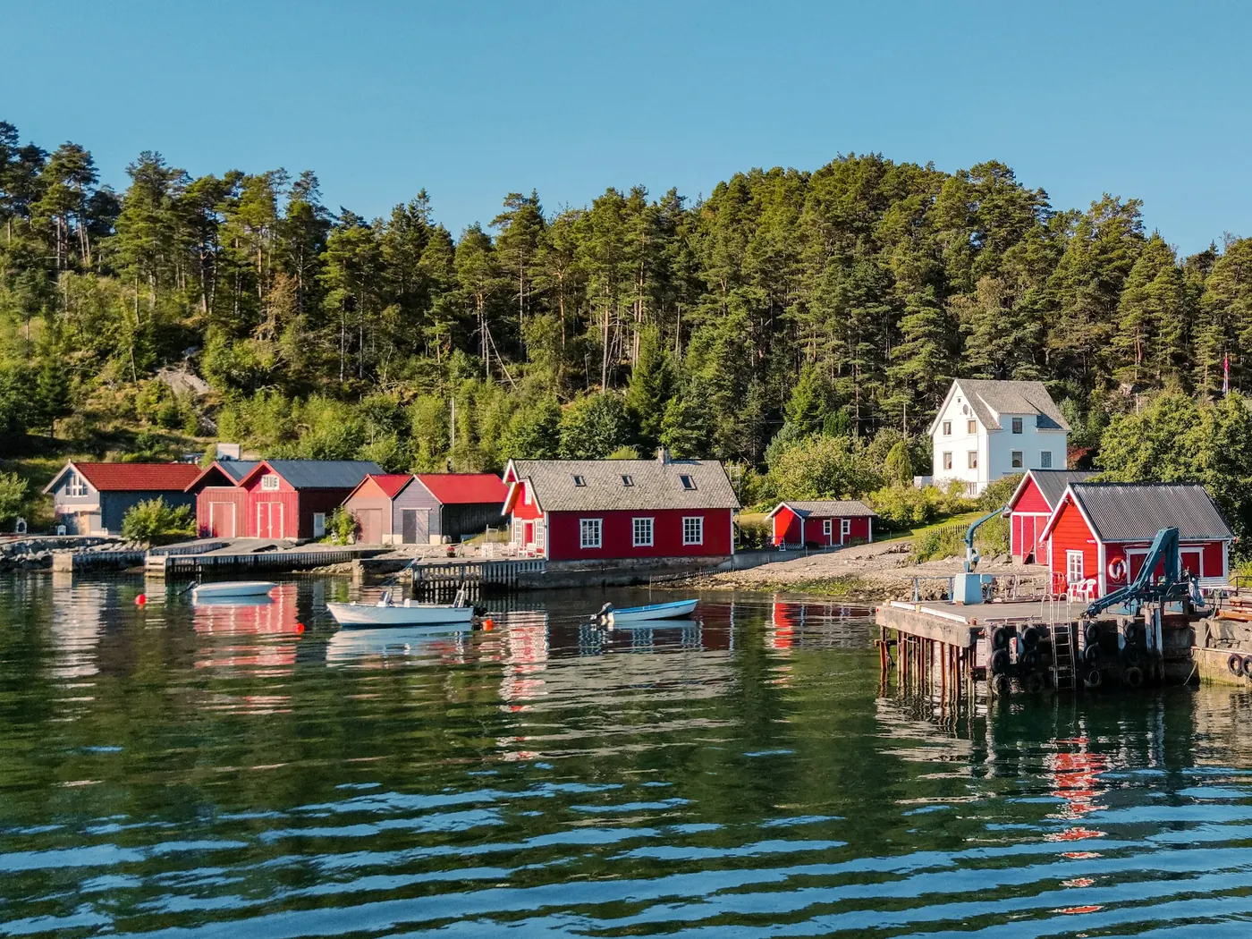 En rekke røde naust og hus ved sjøen som speiler seg i vannet.